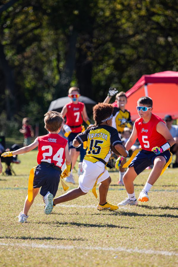 Youth flag football player running with the ball, defenders chasing