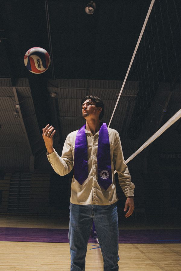 Graduate on a volleyball court tossing a ball